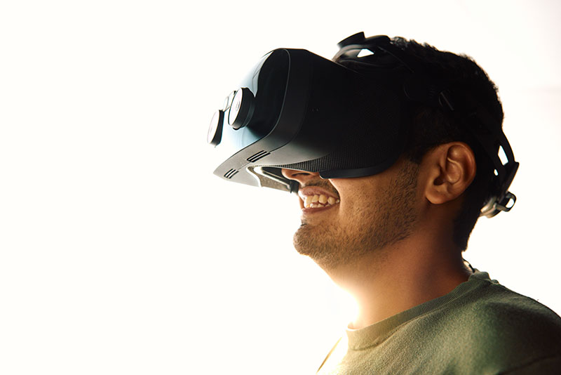 A man with a pair of VR goggles on smiles against a white backdrop. In the photo: Siddharth Rohit Jain, AI Development Engineer, MLOps & AI Development Engineer with ASU Enterprise Technology.
